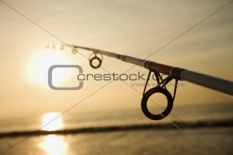 Fishing pole against ocean at sunset.