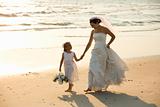 Bride and flower girl walking on beach.