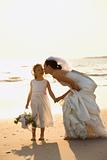 Bride and flower girl holding hands on beach.
