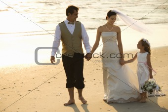 Bride, groom and flower girl walking on beach.