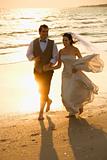 Bride and groom running down beach.