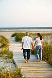 Caucasian couple holding hands on beach walkway.