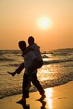 Man carrying woman on beach at sunset.