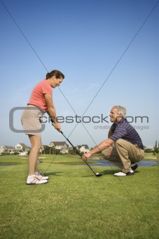 Man teaching woman proper golf techniques.