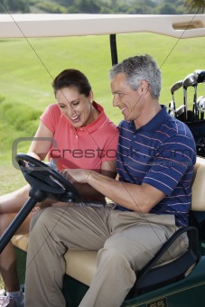 Smiling couple in golf cart on golf course.
