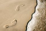 Footprints in sand next to wave.