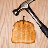 Slice of toast nailed to wood with hammer.