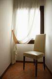 Empty chair by window with drapes.
