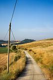 Telephone pole by dirt road and rolling hills in Tuscany, Italy.
