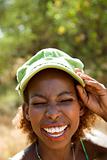 Woman smiling with hand on cap and squinted eyes.