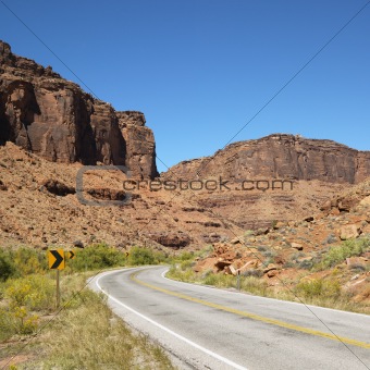 Road curving to right with red rock cliffs in Utah.
