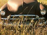 Old abandoned antique car in field.