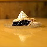 Slice of blueberry pie on plate with whipped topping.