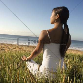 Woman sitting on beach and meditating.