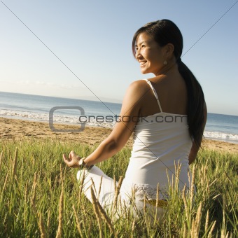 Woman sitting on beach meditating.