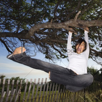 Woman holding on to tree and kicking air.