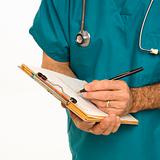 Doctor in scrubs making notes on a patient's chart.