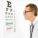 Doctor wearing eyeglasses looking at an eye chart.