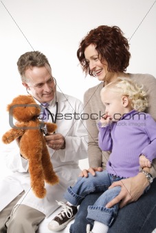 Doctor using teddy bear to demonstrate stethoscope to little gir