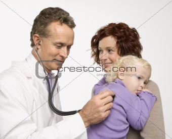 Mother holding her daughter while doctor uses stethoscope.