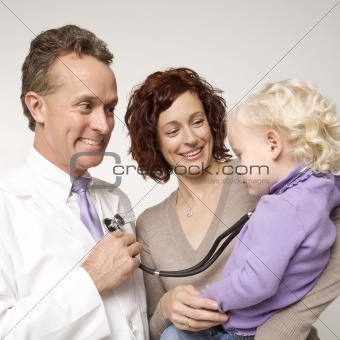 Doctor holding stethoscope as little girl looks on.