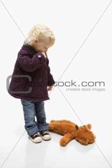 Female toddler looking at her teddy bear on ground.