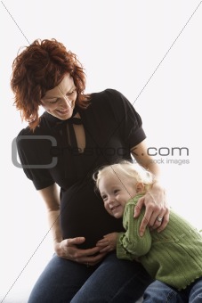 Child with ear against her mother's pregnant belly.