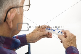 Elderly man holding seven-day pill box.