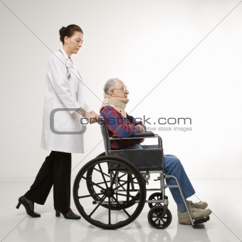 Doctor pushing elderly man with neck brace in wheelchair.