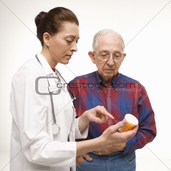 Doctor pointing at prescription bottle as elderly man looks at b