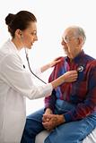 Doctor listening to elderly man's heart with stethoscope.