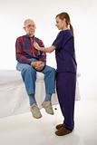 Female in scrubs listening to elderly man's heart.