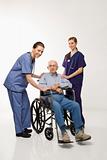Two women wearing scrubs with elderly man in wheelchair.