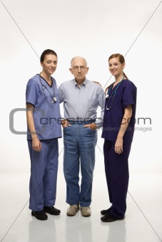 Two women wearing scrubs standing with elderly man.