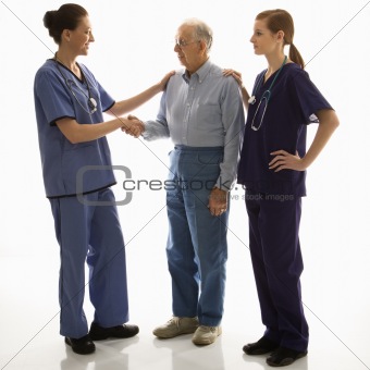 Woman in scrubs shaking hand of elderly man with another woman h