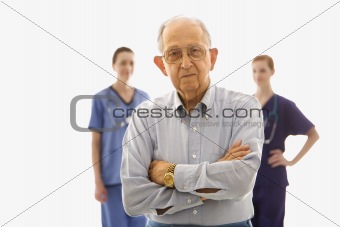 Elderly man in foreground with two nurses in background.