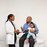Father holding baby talking to pediatrician.