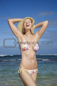 Woman in bikini her holding hat down.