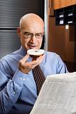 Caucasian businessman eating bagel and reading newspaper.