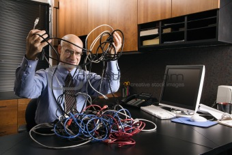 Caucasian businessman with a tangle of computer cables.