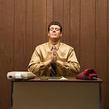 Retro business scene of man praying at desk.