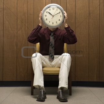 Retro businessman holding clock over face.
