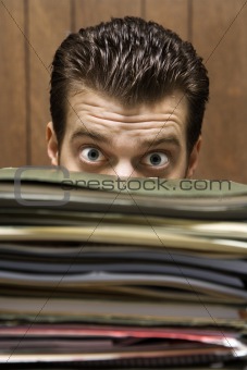 Man peering from behind pile of folders.