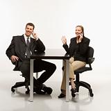 Businessman and woman sitting talking on cell phones.