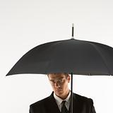 Businessman looking out from under umbrella.