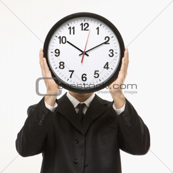Man in suit holding clock in front of face.
