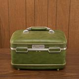 Still life shot of a vintage green luggage piece sitting on a wo