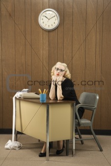 Woman sitting at desk with chin on her fists.