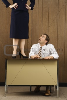Man sitting at desk looking up to woman standing on desk.