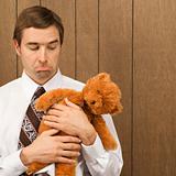 Man holding a stuffed animal looking sad.